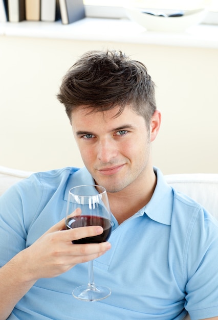 Knappe jonge man zittend op een bank bedrijf wijnglas