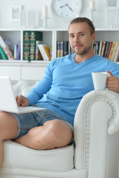 Knappe jonge man zittend op een witte bank met laptop