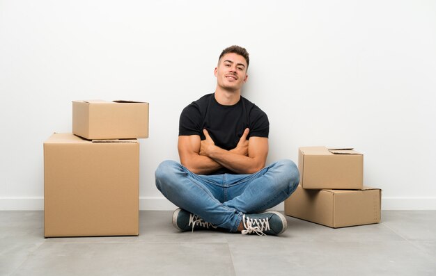 Knappe jonge mens die zich in nieuw huis onder dozen het lachen beweegt