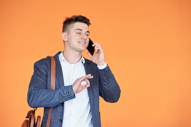 Knappe jonge ondernemer telefonisch met de klant praten en hem overhalen om een deal te sluiten, geïsoleerd op fel oranje