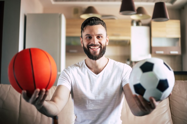 Knappe jonge opgewonden moderne bebaarde man is ontspannen op de bank tijdens het kijken naar voetbalwedstrijd op tv