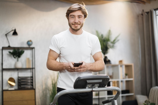 Knappe jonge sportman die telefoon gebruikt en online fitnessles zoekt tijdens het trainen