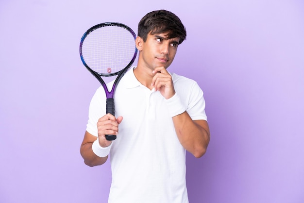 Knappe jonge tennisser man geïsoleerd op oker achtergrond met twijfels en denken