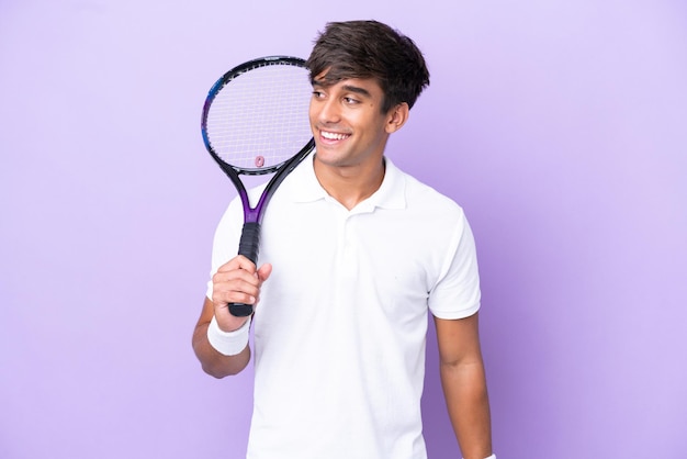 Knappe jonge tennisser man geïsoleerd op oker achtergrond op zoek naar de kant en glimlachend