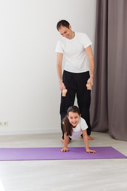 Knappe jonge vader en zijn schattige dochtertje doen reverce plank met beenverhoging op de vloer thuis. Gezinsfitnesstraining.