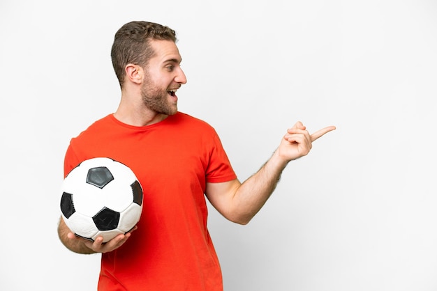 Knappe jonge voetballer man over geïsoleerde witte achtergrond wijzende vinger naar de zijkant en een product presenteren