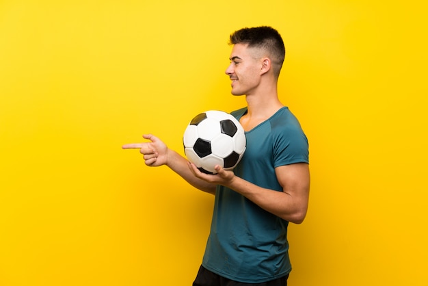 Knappe jonge voetbalstermens die over gele muur aan de kant richten om een product te presenteren