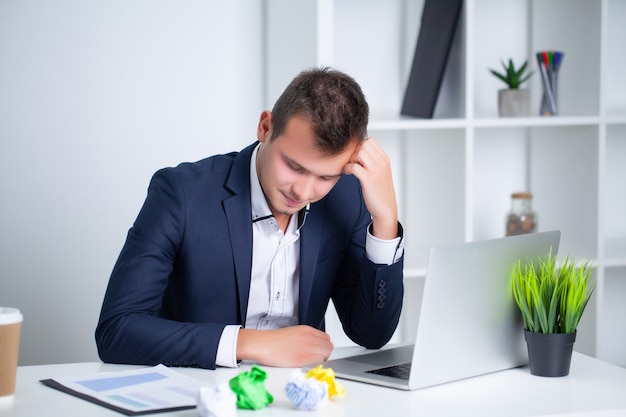 Knappe jonge werknemer die in een bedrijfbureau werkt met documenten en laptop