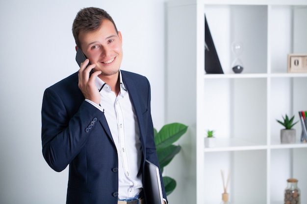 Knappe jonge werknemer maakt gebruik van een telefoon in het bedrijf kantoor