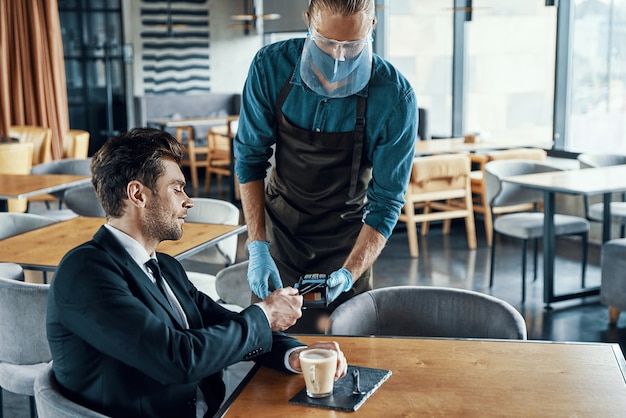 Knappe jonge zakenman die contactloos betaalt terwijl hij in het restaurant zit