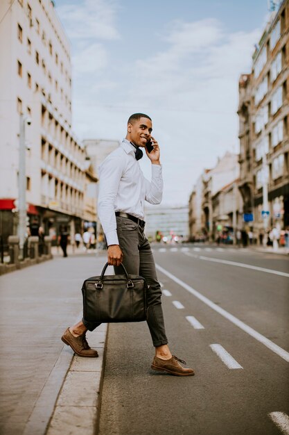 Knappe jonge zakenman die een mobiele telefoon met behulp van tijdens het ceossing een straat