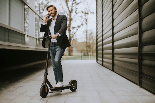 Knappe jonge zakenman die mobiele telefoon op elektrische autoped met behulp van