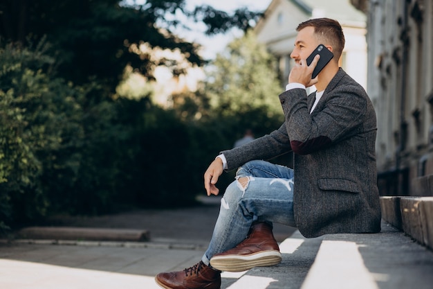 Knappe jonge zakenman die telefoon buiten de straat gebruikt