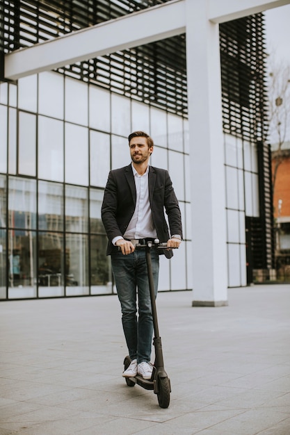 Knappe jonge zakenman in casual kleding rijden op een elektrische scooter door een kantoorgebouw op een zakelijke bijeenkomst