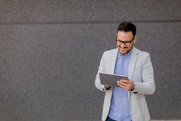 Knappe jonge zakenman met digitale tablet door de grijze muur