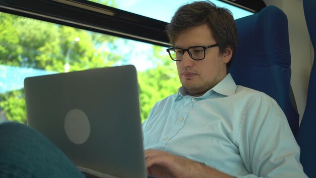 Knappe jonge zakenman met een blauw shirt en bril rijdt in een trein die een nummer kiest en op zijn telefoon praat Zonnige zomerdag