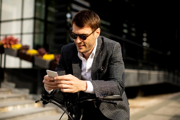 Knappe jonge zakenman op de ebike die mobiele telefoon met behulp van