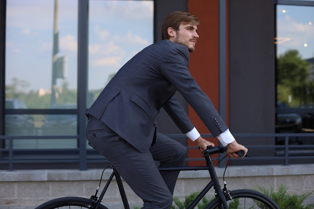 Knappe jonge zakenman rijden op zijn fiets in de stad. Ecologisch vervoersconcept.