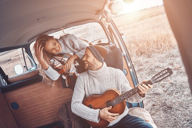 Knappe jongeman die gitaar speelt voor zijn vriendin terwijl hij tijd doorbrengt in de camper