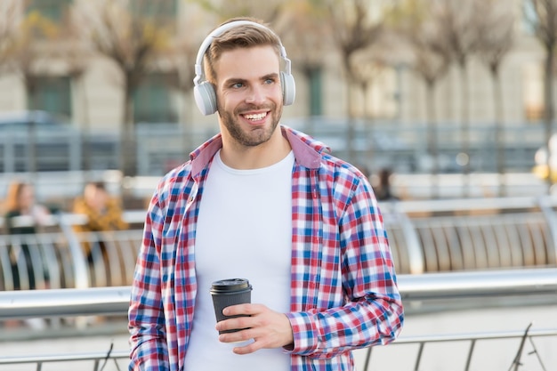 Knappe jongeman draagt een koptelefoon en glimlacht terwijl hij naar muziek luistert en koffie drinkt, inspiratie voor de ochtend