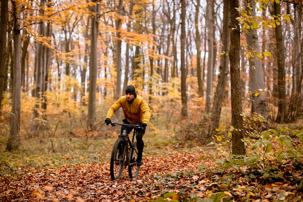 Knappe jongeman fietsen door herfstbos