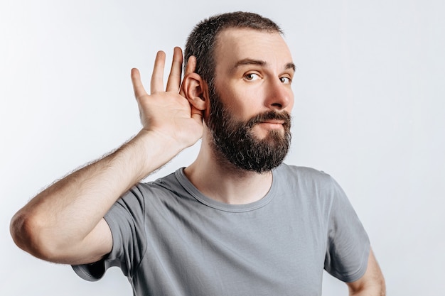 Foto knappe jongeman houdt zijn hand bij zijn oor, wil beter horen op een witte muur