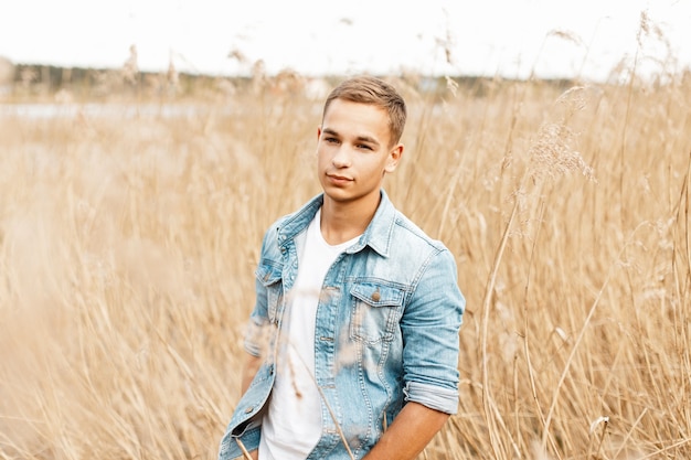 Knappe jongeman in een spijkerjasje en een wit T-shirt in droog gras loopt in de natuur