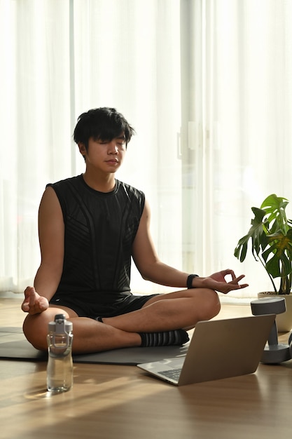 Knappe jongeman in oortelefoons die yoga beoefent in de woonkamer.