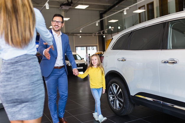 Knappe jongeman met zijn schattige dochtertje die een nieuwe auto kiest in de autoshowroom.