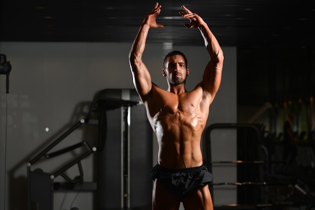 Knappe jongeman staat sterk in de sportschool en buigt spieren Gespierde atletische bodybuilder Fitness Model poseren na oefeningen