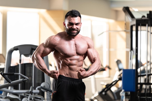 Knappe jongeman staat sterk in de sportschool en buigt spieren Gespierde atletische bodybuilder Fitness Model poseren na oefeningen