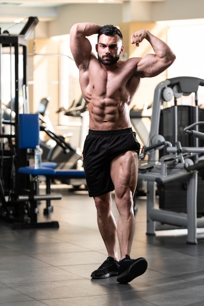 Knappe jongeman staat sterk in de sportschool en buigt spieren Gespierde atletische bodybuilder Fitness Model poseren na oefeningen