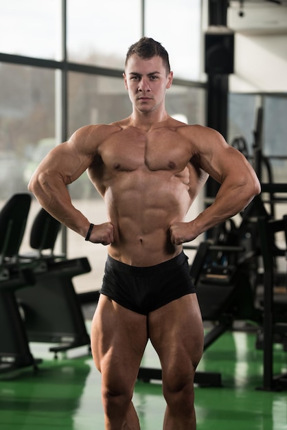 Knappe jongeman staat sterk in de sportschool en buigt spieren Gespierde atletische bodybuilder Fitness Model poseren na oefeningen