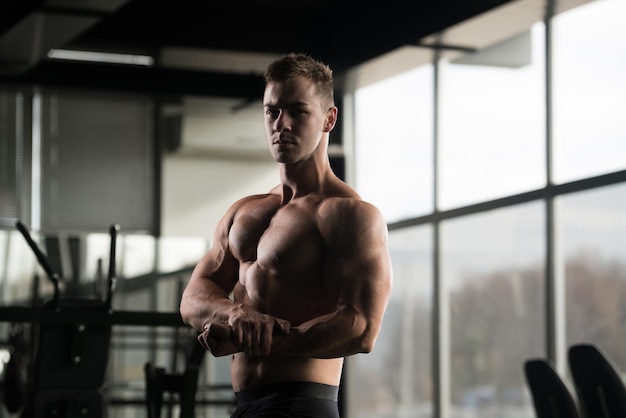 Knappe jongeman staat sterk in de sportschool en buigt spieren Gespierde atletische bodybuilder Fitness Model poseren na oefeningen