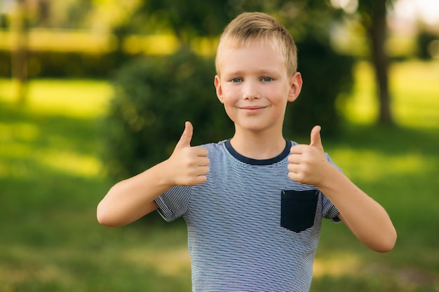 Knappe jongen die en voor de fotograaf glimlacht stelt. Blij kind loopt het park. Zonnig weer zomer.