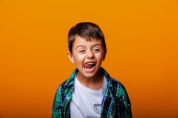 Knappe jongen die tong toont en plezier heeft op een gele achtergrond. Kaukasische emotionele jongen.