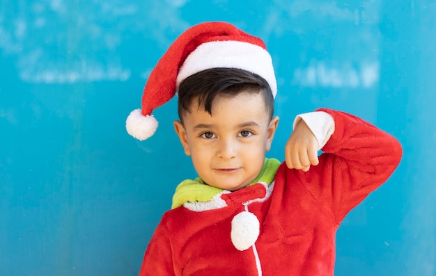 Knappe jongen in het pak van de Kerstman op blauwe muur