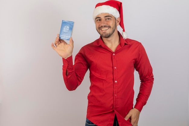 Knappe jongen in kerstkleding en kerstmuts met een Braziliaanse werkkaart Concept van tijdelijke banen voor het einde van het jaar