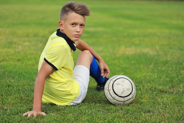 Foto knappe jongen voetballer zittend op het voetbalveld