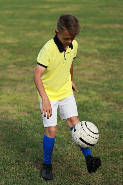 Knappe jongensvoetballer in een geel t-shirt op het voetbalveld jongleert met de bal