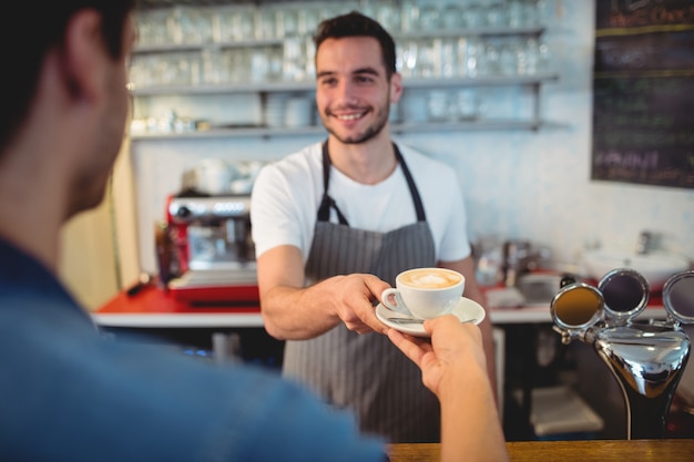 Knappe kelners dienende koffie aan mannelijke klant bij cafetaria