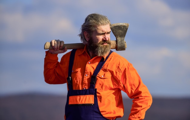 Knappe kerel brutaal humeur Professionele bezetting Man in uniform houdt bijl vast Brutale bebaarde man bijl in handen Brutale en bebaarde Bouwer met bijl Dwangarbeid Gebruik bijlconstructie Renovatietools