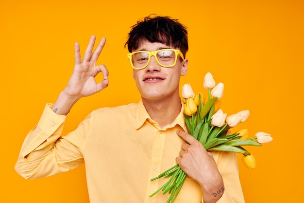 Knappe kerel geeft bloemen draagt een bril geel shirt geïsoleerde achtergrond ongewijzigd
