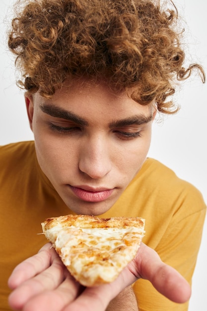 Knappe kerel in een gele t-shirt die pizza geïsoleerde achtergrond eet