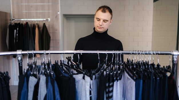 Knappe klant in zwarte golf probeert wat kleding te vinden voor herfst- en winterkleding voor het nieuwe seizoen