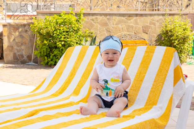 Knappe kleine jongen in zonnebril en een bandana zit op een ligstoel bij het zwembad. Selectieve aandacht.