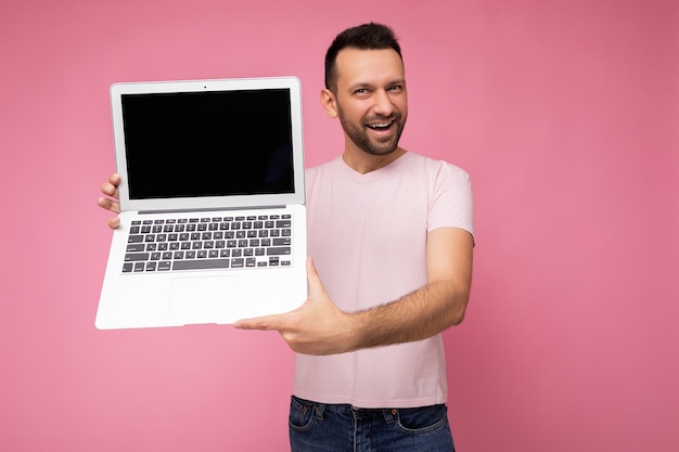 Knappe lachende brunet man met laptopcomputer kijken camera in t-shirt