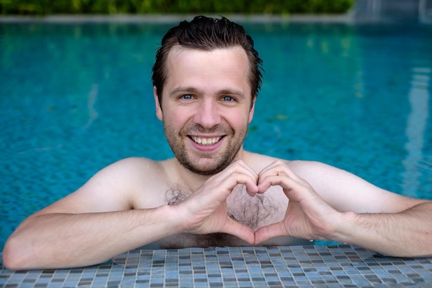 Knappe lachende jonge blanke man maakt het hart met vingers handen tijdens het zwemmen bij het zwembad