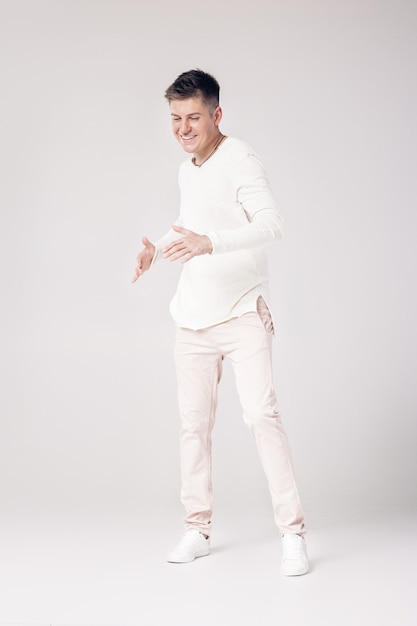 Knappe lachende jonge man in een witte trui en broek
