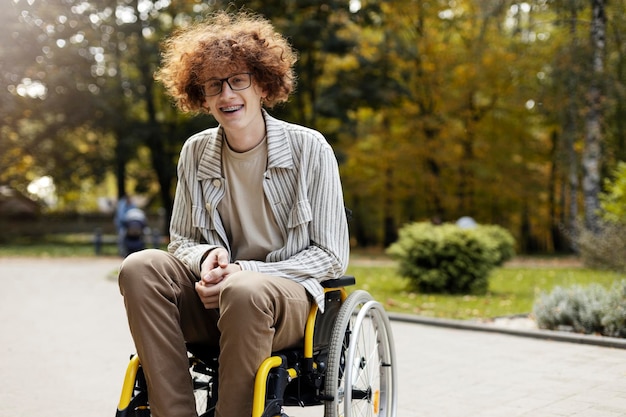 Knappe lachende man met bril en beugel een man zit in een rolstoel in een park buiten